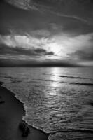 Sonnenuntergang beim das Meer im schwarz und Weiß verträumt. sandig Strand im das Vordergrund foto