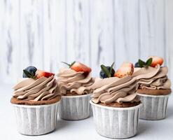 Gruppe von Schokolade Cupcakes mit Sahne Käse Glasur, Erdbeere und Blaubeere auf hölzern Hintergrund foto