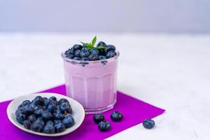 lecker frisch Blaubeere Joghurt Shake Dessert im Glas Stehen auf Weiß Tabelle lila Serviette Hintergrund. foto