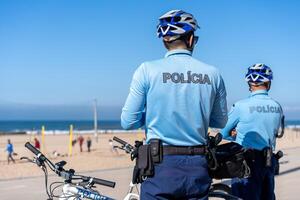 zwei Polizist patrouillieren Strand Promenade auf Fahrräder. Menschen sind Sonnenbrand auf das Stadt Öffentlichkeit Strand auf das atlantisch Ufer. foto