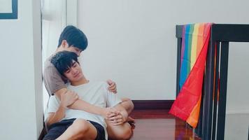 asiatisches schwules Paar, das zu Hause auf dem Boden liegt und umarmt. junge asiatische lgbtq-männer, die sich glücklich küssen, entspannen sich zusammen und verbringen morgens romantische zeit im wohnzimmer mit regenbogenflagge im modernen haus. foto