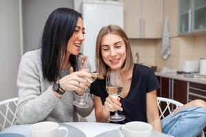 freunde Treffen mit Wein und Kuchen im das modern Stil Küche. jung Frauen Lächeln und Scherz mit Brille von Wein im seine Hände foto