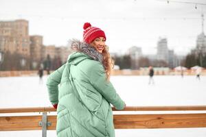 schön schön mittleren Alters Mädchen mit lockig Haar warm Winter Jacken steht Eis Eisbahn Hintergrund Stadt, Dorf Quadrat. foto