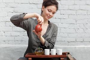 ein Mädchen im ein grau Leinen- Hemd arrangiert ein königlich Zeremonie, klassisch Zubehör zum ein Tee Zeremonie. Konzept von gesund Essen und traditionell Getränke foto