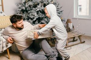 Urlaub Weihnachten gut aussehend Vater spielen mit klein süß Sohn in der Nähe von dekoriert Neu Jahr Baum beim Zuhause foto