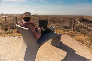 Frau mit Laptop Computer Sitzung im Vorderseite von das Strand im Barcelona. foto