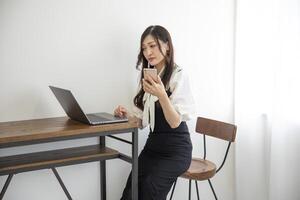 ein japanisch Frau Überprüfung Smartphone durch Fernbedienung Arbeit im das Zuhause Büro foto