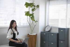 ein japanisch Frau Überprüfung Smartphone durch Fernbedienung Arbeit im das Zuhause Büro foto