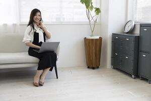 ein japanisch Frau Überprüfung Smartphone durch Fernbedienung Arbeit im das Zuhause Büro foto