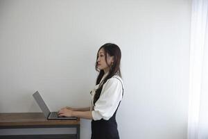 ein japanisch Frau Überprüfung Smartphone durch Fernbedienung Arbeit im das Zuhause Büro foto