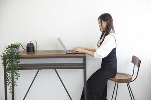 ein japanisch Frau Überprüfung Smartphone durch Fernbedienung Arbeit im das Zuhause Büro foto