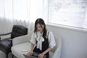 ein japanisch Frau Überprüfung Smartphone durch Fernbedienung Arbeit im das Zuhause Büro foto