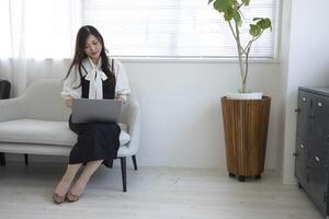 ein japanisch Frau Überprüfung Smartphone durch Fernbedienung Arbeit im das Zuhause Büro foto