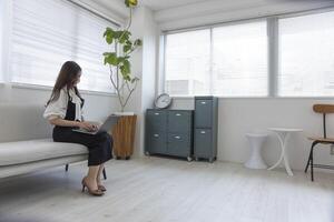 ein japanisch Frau Überprüfung Smartphone durch Fernbedienung Arbeit im das Zuhause Büro foto