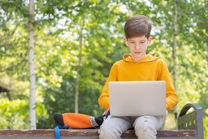 nachdenklich Teenager Junge Arbeiten auf Laptop. halten und mit ein Laptop zum Vernetzung auf ein sonnig Frühling Tag, draußen. foto