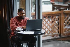 afrikanisch amerikanisch Mann Arbeiten auf Laptop im ein Cafe. foto