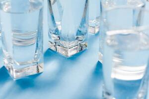 Linie von Gläser, ein Glas mit Wasser, auf ein Licht Blau Hintergrund. Unterschied Konzept. Gleichberechtigung Konzept. foto