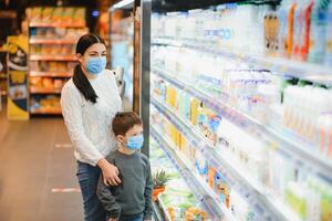 jung Frau und ihr Kind tragen schützend Gesicht Masken Geschäft ein Essen beim ein Supermarkt während das Coronavirus Epidemie oder Grippe Ausbruch. foto