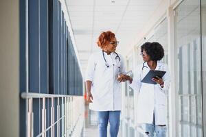 Porträt zuversichtlich afrikanisch amerikanisch weiblich Arzt medizinisch Fachmann Schreiben geduldig Anmerkungen isoliert auf Krankenhaus Klinik Flur Fenster Hintergrund. positiv Gesicht Ausdruck foto