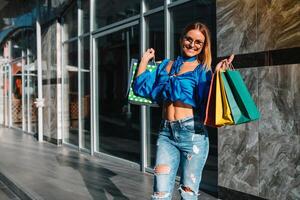 lächelnd jung Frau posieren mit ein Hand voll von Einkaufen Taschen. Einkaufen Konzept. foto