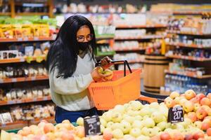 afrikanisch Frau tragen Einweg medizinisch Maske. Einkaufen im Supermarkt während Coronavirus Pandämie Ausbruch. Epidemie Zeit foto