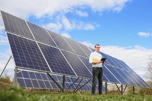 Solar- Energie. jung Geschäft Mann im ein Weiß Hemd in der Nähe von das Solar- Paneele zu Leistung Pflanzen. foto