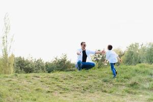 gut aussehend Papa mit seine wenig süß Sohn sind haben Spaß und spielen auf Grün grasig Rasen. glücklich Familie Konzept. Schönheit Natur Szene mit Familie draussen Lebensstil. Familie ruhen zusammen. Väter Tag foto