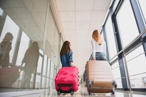 glücklich jung Mutter und ihr Tochter Gehen im das Flughafen Terminal während Tragen ein Koffer. hoch Jahreszeit und Ferien Konzept. entspannen und Lebensstile foto