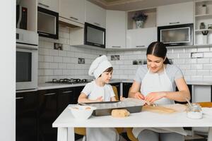 wenig Junge Portion seine Mutter mit das Backen im das Küche Stehen beim das Zähler neben ihr kneten das Teig zum das Kuchen foto