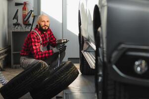 Auto Mechaniker Schrauben oder abschrauben Auto Rad von angehoben Automobil durch pneumatisch Schlüssel beim Reparatur Bedienung Bahnhof foto