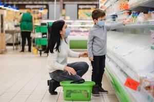 authentisch Schuss von Mutter und Sohn tragen medizinisch Masken zu schützen sich von Krankheit während Einkaufen zum Lebensmittel zusammen im Supermarkt foto