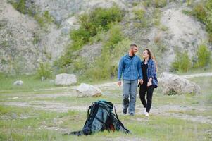 Paar von jung glücklich Reisende Wandern mit Rucksäcke auf das schön felsig Weg beim warm sonnig Abend. Familie Reise und Abenteuer Konzept. foto