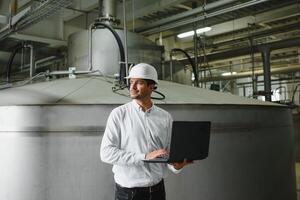 lächelnd und glücklich Mitarbeiter. industriell Arbeiter drinnen im Fabrik. jung Techniker mit Weiß schwer Hut. foto