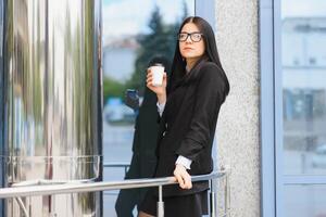 Porträt von erfolgreich Geschäft Frau gehen zu Arbeit mit Kaffee Gehen in der Nähe von Büro Gebäude auf Stadt Straße. foto