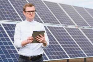 Solar- Energie. jung Geschäft Mann im ein Weiß Hemd in der Nähe von das Solar- Paneele zu Leistung Pflanzen. foto