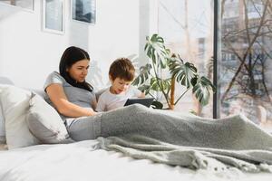 schön lächelnd Mutter und Sohn spielen mit Digital Tablette Verlegung auf Bett. foto