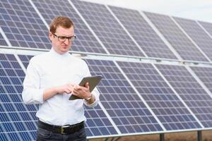 Solar- Energie. jung Geschäft Mann im ein Weiß Hemd in der Nähe von das Solar- Paneele zu Leistung Pflanzen. foto