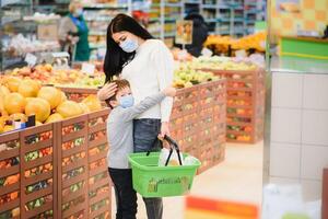 jung Frau und ihr Kind tragen schützend Gesicht Masken Geschäft ein Essen beim ein Supermarkt während das Coronavirus Epidemie oder Grippe Ausbruch. foto