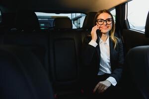 schön erfolgreich Geschäftsfrau sich unterhalten auf ihr Handy, Mobiltelefon Telefon im ein Rücksitz von ein Auto foto