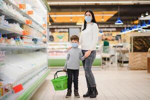 Porträt von ein Mutter und ihr wenig Sohn tragen schützend Gesicht Maske beim ein Supermarkt während das Coronavirus Epidemie oder Grippe Ausbruch. leeren Raum zum Text foto