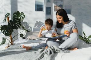 Mama mit Sohn im Pyjama Trinken Saft im das Morgen im Bett. gesund Essen Konzept foto