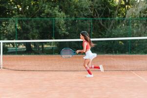 Kind spielen Tennis auf draussen Gericht. wenig Mädchen mit Tennis Schläger und Ball im Sport Verein. aktiv Übung zum Kinder. Sommer- Aktivitäten zum Kinder. Ausbildung zum jung Kind. Kind Lernen zu abspielen foto