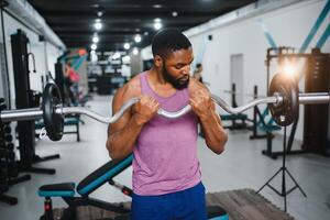 muskulös Mann tun Gewicht Heben Übung beim Fitnessstudio mit Kopieren Raum. Seite Aussicht von passen afrikanisch amerikanisch Kerl Stehen mit schwer Gewicht auf Hantel beim Crossfit Verein. reifen Mann Arbeiten auf Bizeps beim Fitnessstudio. foto