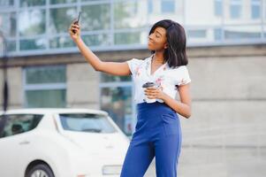 gut suchen afrikanisch weiblich posiert beim Kamera von Zelle Telefon, macht Selfie oder macht Video Anruf foto