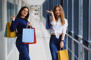 glücklich zwei kaukasisch Frauen sind tun Einkaufen zusammen beim das Einkaufszentrum Center. zwei jung Frauen sind Gehen mit Einkaufen Taschen beim Einkaufszentrum. foto