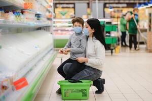 Porträt von ein Mutter und ihr wenig Sohn tragen schützend Gesicht Maske beim ein Supermarkt während das Coronavirus Epidemie oder Grippe Ausbruch. leeren Raum zum Text foto