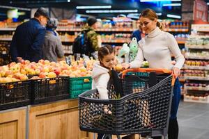 Familie im das Supermarkt. schön jung Mama und ihr wenig Tochter lächelnd und Kauf Lebensmittel. das Konzept von gesund Essen. Ernte foto