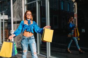 lächelnd jung Frau posieren mit ein Hand voll von Einkaufen Taschen foto