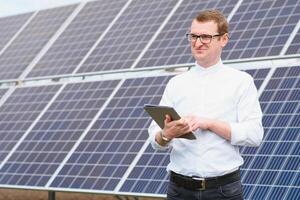 Solar- Energie. jung Geschäft Mann im ein Weiß Hemd in der Nähe von das Solar- Paneele zu Leistung Pflanzen. foto