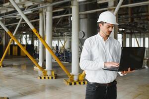 lächelnd und glücklich Mitarbeiter. industriell Arbeiter drinnen im Fabrik. jung Techniker mit Weiß schwer Hut. foto